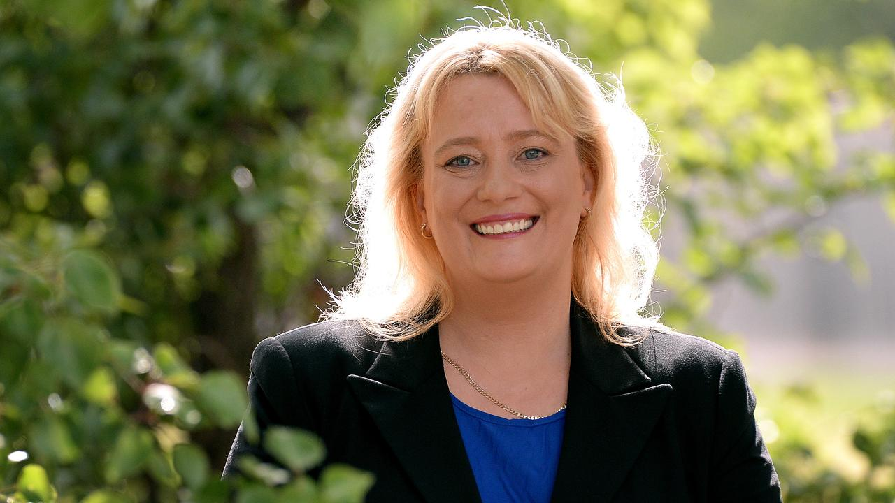 Ros Spence is standing in front of some outdoor greenery. She has shoulder-length blonde hair and is wearing a blue top underneath a black blazer.