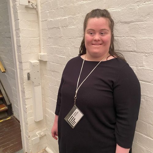 Amelia volunteering at fortyfivedownstairs. She is wearing a black dress with long sleeves and a lanyard around her neck.