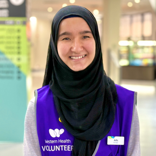 A close up of Arifa at Western Health. She is wearing a black hijab and purple 'Volunteer' vest.