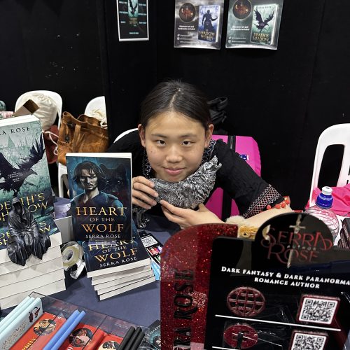 Jessica volunteering at a book fair event. She is sitting at a table full of books and memorabillia.