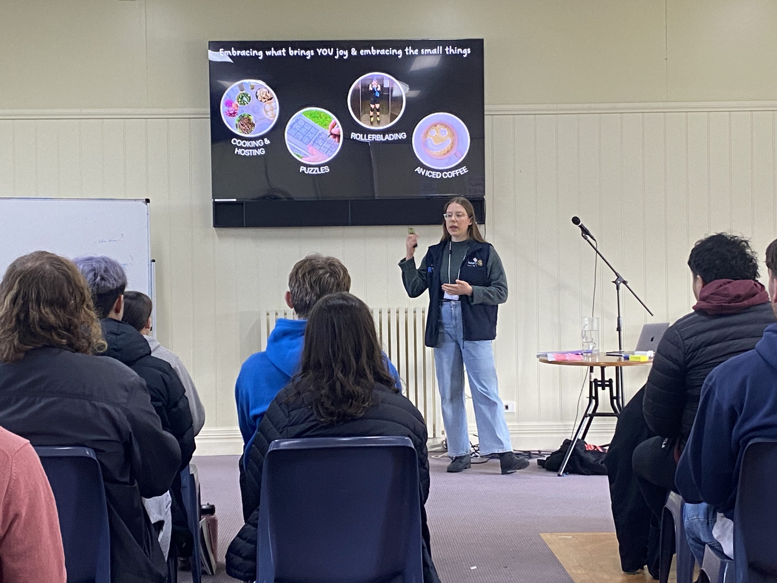 Christine presenting to a room of young people. She is standing in front of a large screen, pointing.